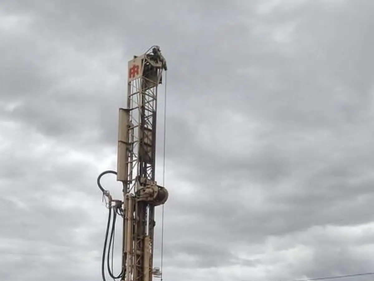 The drill mast raised against a storm sky